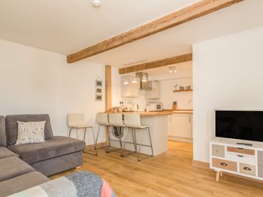 A living room with a gray sofa and kitchen with bar stools at Potters by the Sea in Sennen