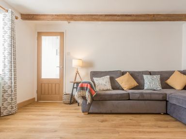 A living room with a gray sofa and cushions a wooden door and a floor lamp at Potters by the Sea in Sennen