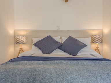 A bedroom with a double bed and two blue pillows and two bedside lamps with patterned shades at Potters by the Sea in Sennen