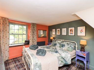A bedroom with a double bed with plant patterned bedding bedside tables with lamps framed pictures on the wall and a window with curtains at Bonny Bits Cottage in Garrigill near Alston