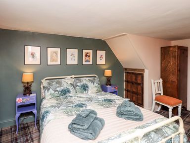 A bedroom with a double bed with patterned bedding two bedside tables with lamps and wall art above the bed at Bonny Bits Cottage in Garrigill near Alston