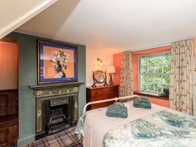 A bedroom with a bed folded towels on it a fireplace a dresser with a mirror and a window with curtains at Bonny Bits Cottage in Garrigill near Alston
