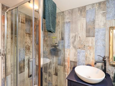 A bathroom with a glass shower enclosure a towel hanging above wooden panel walls and a sink with a faucet at Bonny Bits Cottage in Garrigill near Alston