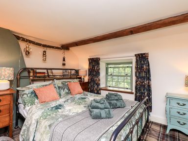 A bedroom with a double bed with floral bedding and pillows beside wooden nightstands and a window at Bonny Bits Cottage Garrigill near Alston