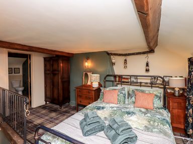 A bedroom with a bed with folded towels bedside tables a wardrobe and a view into a bathroom at Bonny Bits Cottage in Garrigill near Alston