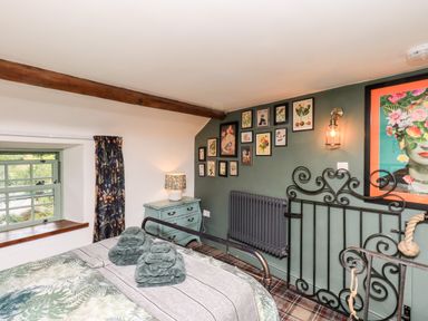 A bedroom with an iron bed frame and a green chest of drawers under a floral lamp at Bonny Bits Cottage in Garrigill near Alston