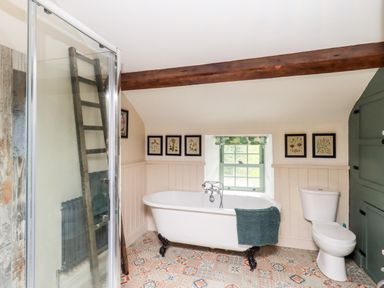 A bathroom with a freestanding bathtub a toilet a shower enclosure and framed pictures on the wall at Bonny Bits Cottage in Garrigill near Alston