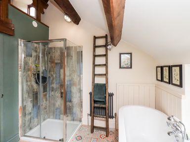 A bathroom with a glass shower enclosure wooden ladder with towels freestanding bathtub and framed pictures at Bonny Bits Cottage in Garrigill near Alston