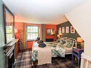 A bedroom with a bed with floral bedding two bedside tables with lamps a window with curtains and a fireplace at Bonny Bits Cottage in Garrigill near Alston