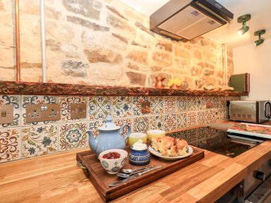 A kitchen countertop with a wooden tray holding a teapot cups scones jam and cream in Bonny Bits Cottage in Garrigill near Alston