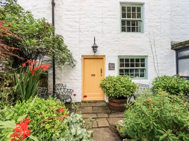 Front view of a white cottage with a yellow door green windows plants and metal chairs at Bonny Bits Cottage Garrigill near Alston