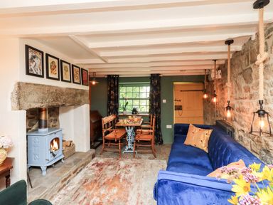 A living room with a blue sofa a wood stove a wooden dining table with chairs and hanging pendant lights at Bonny Bits Cottage in Garrigill near Alston