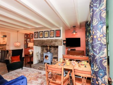 A living room with a wood stove fireplace dining table with food and chairs a patterned curtain and a television at Bonny Bits Cottage in Garrigill near Alston