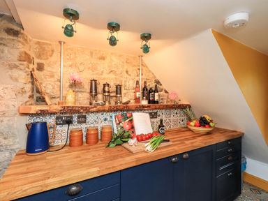 A kitchen countertop with a blue kettle jars vegetables bottles and a fruit bowl at Bonny Bits Cottage in Garrigill near Alston