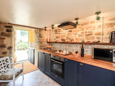 A kitchen with stone walls blue cabinets a wooden countertop and a chair at Bonny Bits Cottage in Garrigill near Alston