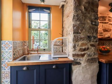 A kitchen sink with a copper faucet below a window next to a stone wall at Bonny Bits Cottage in Garrigill near Alston