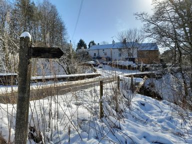 A snowy rural road with a wooden signpost and buildings in the distance at Bonny Bits Cottage in Garrigill near Alston