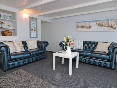 A living room with two blue leather sofas a white table with flowers and a wall painting at Pebble Cottage in Portreath