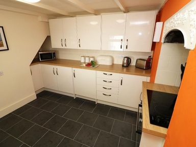 A kitchen with white cabinets wooden countertops a microwave kettle toaster and an electric stove at Pebble Cottage in Portreath