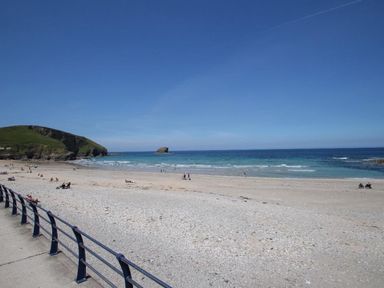 A beach with people on the sand and in the water near a grassy hill at Pebble Cottage in Portreath
