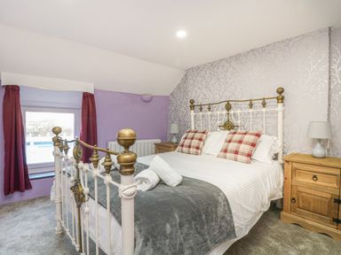 A bedroom with a metal bed, checked pillows, nightstands with lamps and a window with red curtains at Pebble Cottage in Portreath