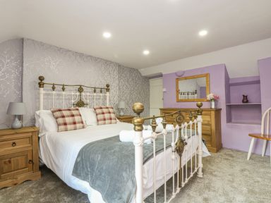 A bedroom with a metal bed frame plaid pillows wooden nightstands with lamps a wooden dresser mirror and a chair at Pebble Cottage in Portreath