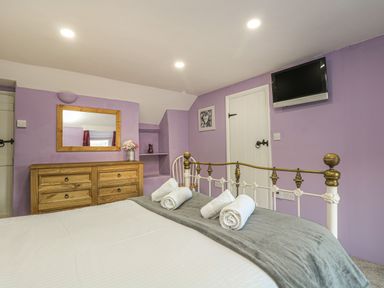 A bedroom with a metal bed frame wooden dresser with a mirror on the wall and a wall-mounted TV at Pebble Cottage in Portreath