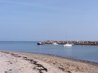 A beach with pebbles and seaweed with boats anchored near a rocky breakwater at Sea Breeze in Rhos-on-Sea