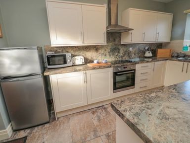 A kitchen with white cabinets a stainless steel fridge a microwave a toaster an oven a kettle and countertop at Forge Cottage in Rothbury