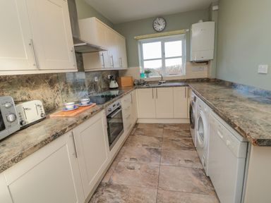 A kitchen with white cabinets marble countertops washing machine and dishwasher at Forge Cottage in Rothbury