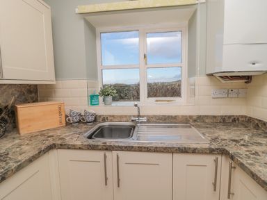 A kitchen sink with marble countertops cups and a breadbox on the counter at Forge Cottage in Rothbury