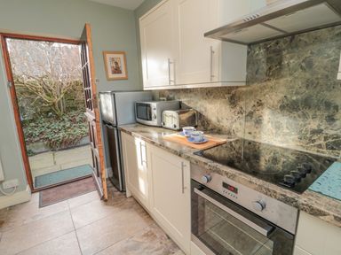 A kitchen with white cabinets a countertop with microwave toaster and cups and an open door leading outside at Forge Cottage in Rothbury