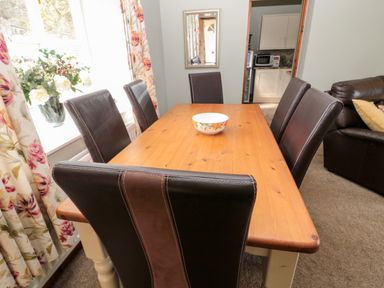 A dining area with a wooden table and six brown chairs a bowl on the table floral curtains and a flower vase on the windowsill Forge Cottage Rothbury