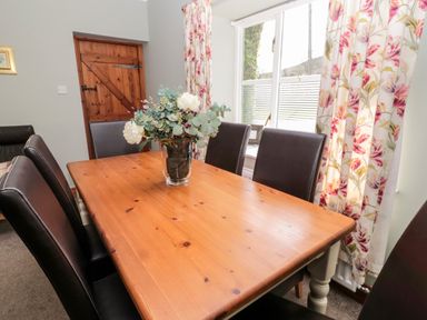 A dining room with a wooden table and black chairs a flower vase on the table and floral curtains at Forge Cottage in Rothbury