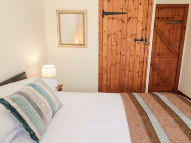 A bedroom with a bed with striped pillows a bedside table with a lamp and two wooden doors at Forge Cottage in Rothbury