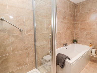 A bathroom with a bathtub and a shower area with stacked towels and a towel on the tub edge at Forge Cottage in Rothbury