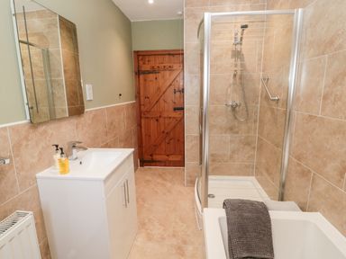 A bathroom with a white sink cabinet a curved glass shower enclosure a wooden door and beige tiled walls at Forge Cottage in Rothbury