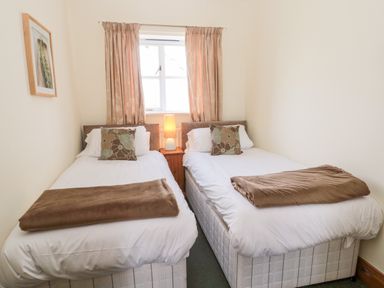 A bedroom with two single beds a nightstand a lamp curtains and a framed picture on the wall at Forge Cottage in Rothbury
