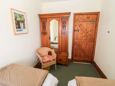 A room with two single beds a wooden wardrobe a wicker chair and a wooden door at Forge Cottage in Rothbury