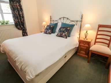 A bedroom with a double bed with pillows bedside tables with lamps a wooden chair and a window with curtains at Forge Cottage in Rothbury