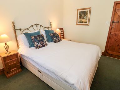 A bedroom with a bed with decorative pillows two wooden nightstands with lamps a framed picture on the wall and a wooden door at Forge Cottage in Rothbury