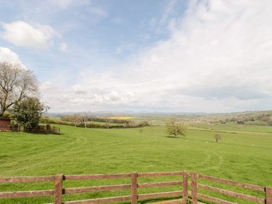 A large green field with grazing sheep and a wooden fence in the foreground at Forge Cottage in Rothbury