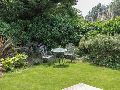 A garden with two metal chairs and a round metal table on grass surrounded by bushes at The Coach House in Teignmouth