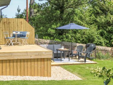 A garden with wooden decking and outdoor seating including chairs table and umbrella at The Coach House in Teignmouth