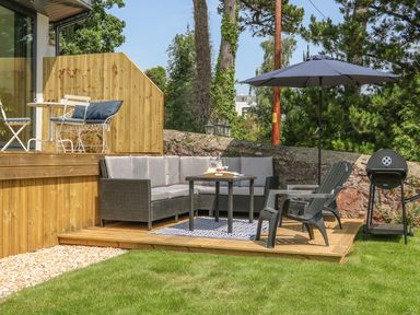 An outdoor seating area with a sectional sofa table umbrella chairs and a barbecue grill at The Coach House in Teignmouth