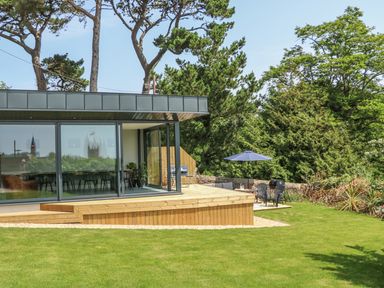 A garden with green grass trees a wooden deck table with umbrella and chairs at The Coach House in Teignmouth