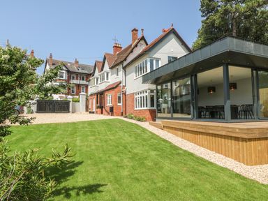 A garden with a grass lawn and a modern glass extension attached to a traditional house at The Coach House in Teignmouth