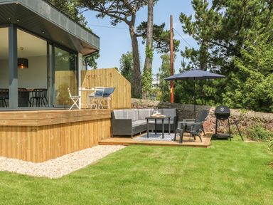 A backyard with wooden patio furniture including a sofa table umbrella and grill at The Coach House in Teignmouth