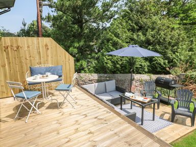 An outdoor wooden deck with seating areas including chairs and a table under an umbrella at The Coach House in Teignmouth