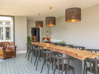 A dining room with a long wooden table surrounded by black chairs and three hanging lamps at The Coach House in Teignmouth